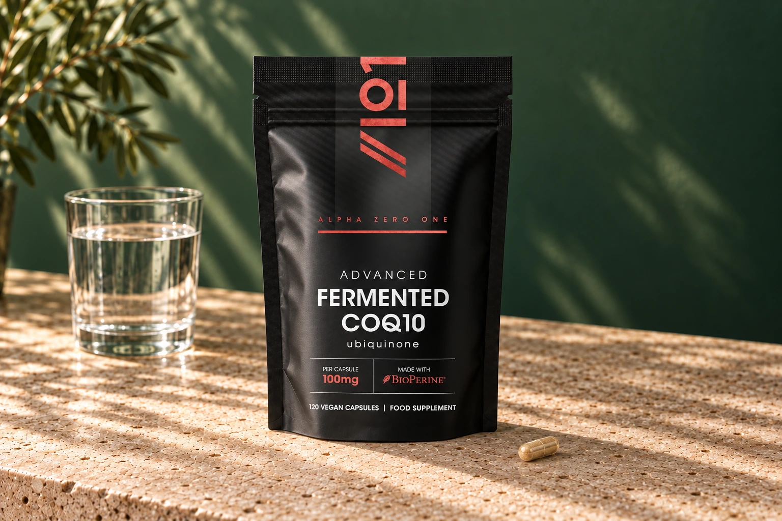 Alpha01 Fermented CoQ10 100mg 120 vegan capsules pouch with one tan-filled hard capsule and a glass of water on stone