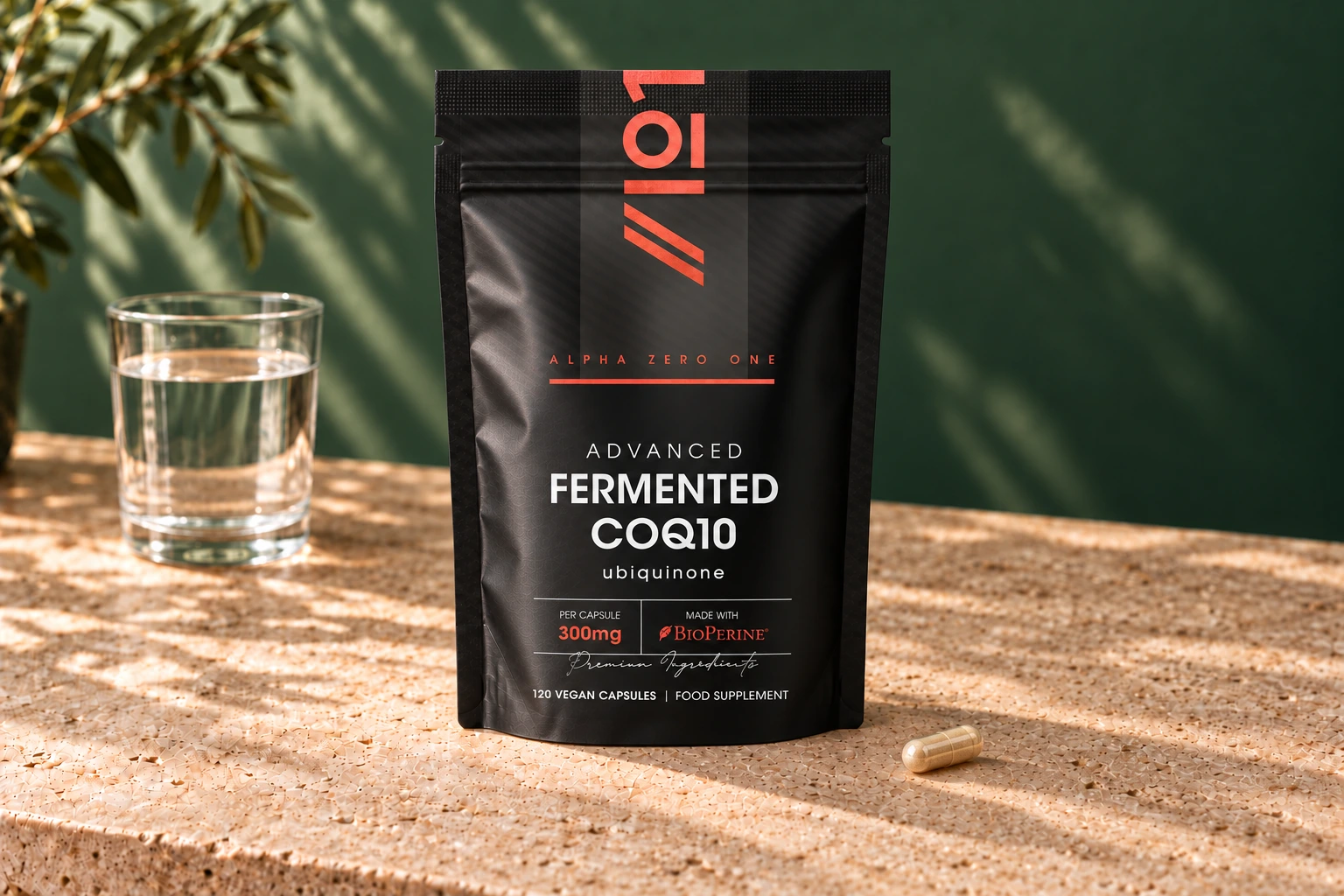 Alpha01 Fermented CoQ10 300mg 120 vegan capsules pouch with one tan-filled hard capsule and a glass of water on stone